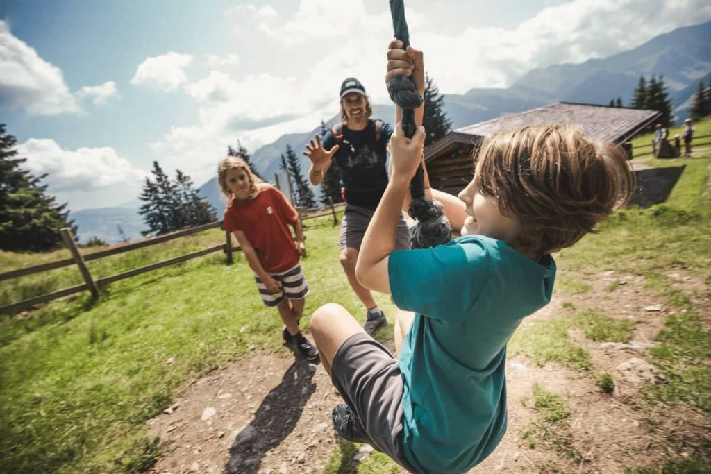 Kinder spielen im Freien an einer Seilbahn vor Bergkulisse in Saalbach-Hinterglemm.
