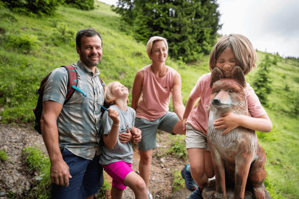 Familie genießt den Sommerurlaub in den Bergen, posiert vor einer Fuchs-Skulptur.