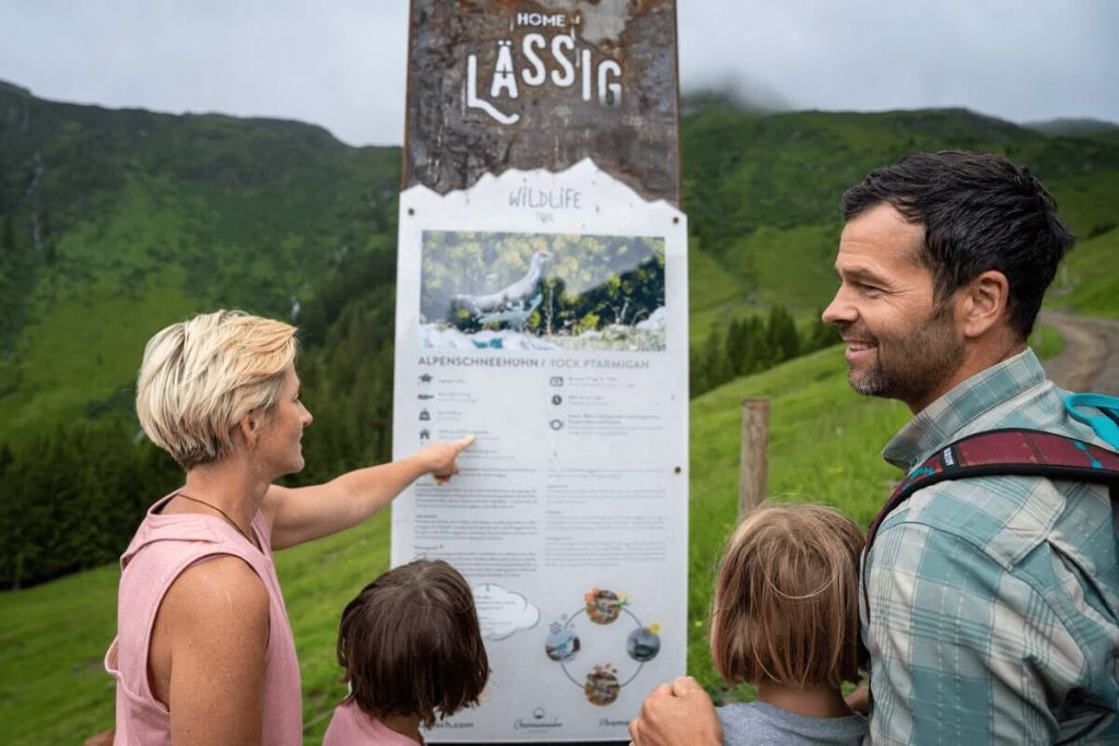 Familie steht an einem Informationsschild über die Tierwelt in den Bergen von Saalbach.