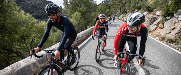 Cyclists in Sportswear on a Road Surrounded by Trees and Rocks.