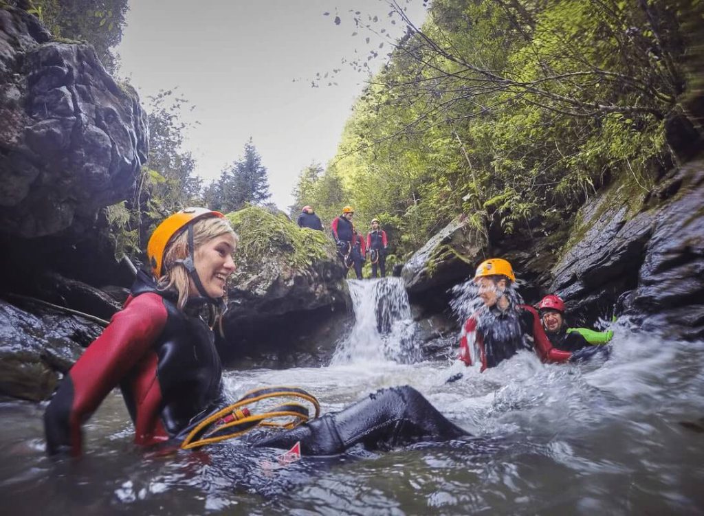 Gruppe beim Canyoning mit Wasserfall in den Bergen, umgeben von üppiger Natur.
