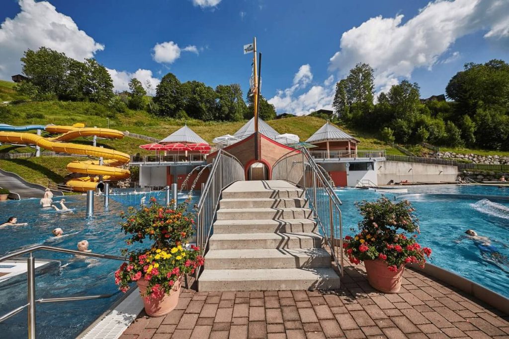 Blick auf das Freibad mit Rutschen und Bäumen an einem sonnigen Tag in Saalbach-Hinterglemm.