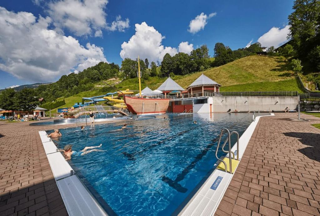 Blick auf den Außenpool mit Wasserrutschen und grünen Hügeln in Saalbach-Hinterglemm.