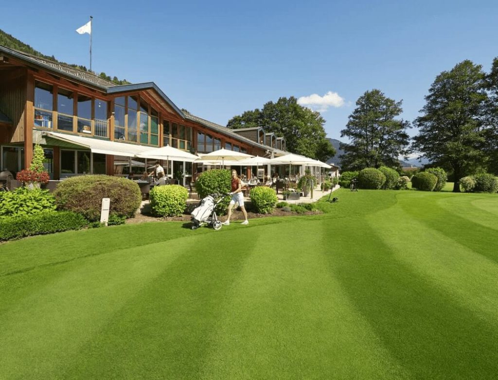 Hotel Wolfgang mit Gartenanlage, Sonnenschirmen und Golfausrüstung im Vordergrund.