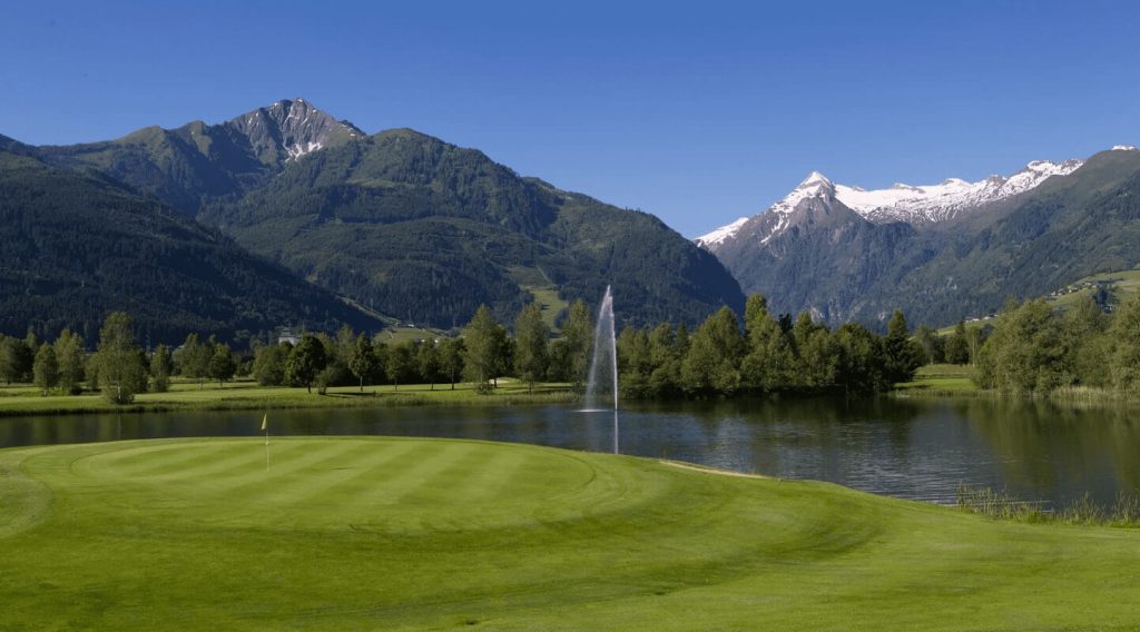 Golfplatz mit Teich, Bergen im Hintergrund und klarem blauen Himmel in Saalbach-Hinterglemm.