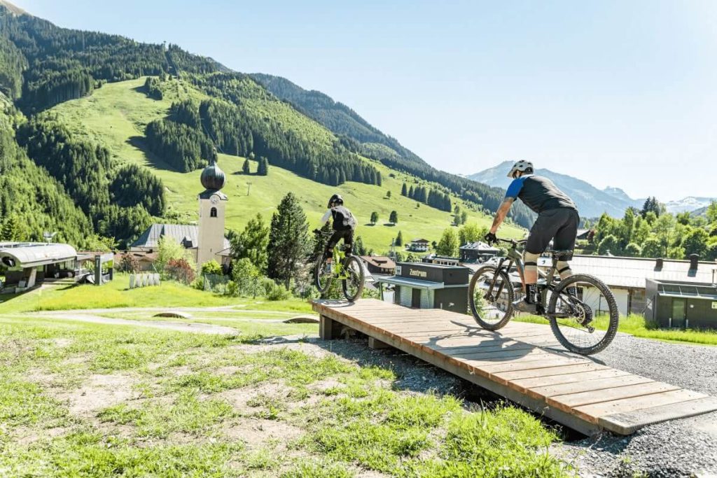 Mountainbiker auf einer Holzrampe mit bergiger Kulisse in Saalbach-Hinterglemm.
