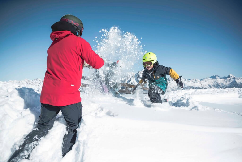 Zwei Skifahrer im Schnee haben Spaß und sorgen für Schneeflocken im Sonnenlicht.