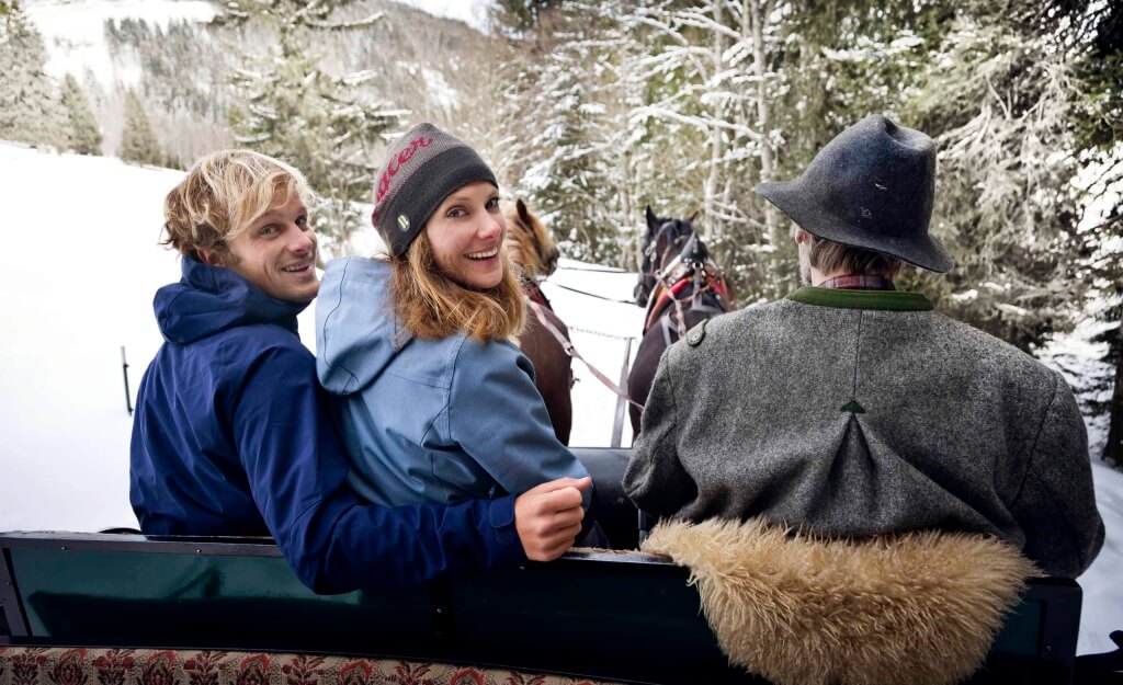 Pärchen im Pferdeschlitten durch verschneite Berge in Saalbach-Hinterglemm.