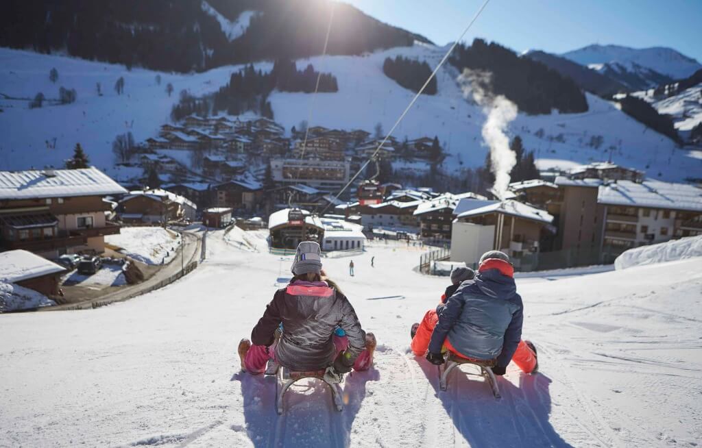 Zwei Personen auf Schlitten auf einer verschneiten Piste in Saalbach-Hinterglemm.