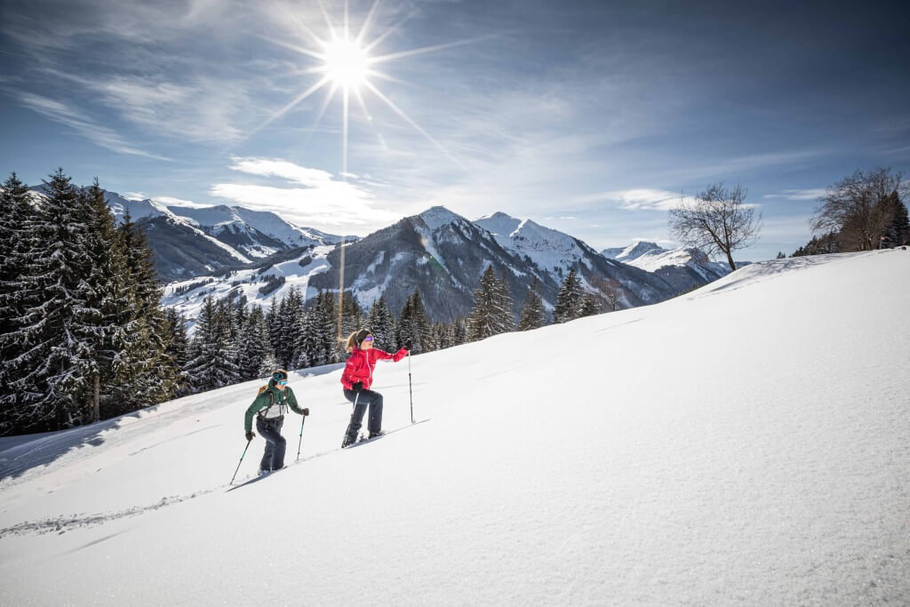 Zwei Personen wandern durch verschneite Berglandschaft bei Sonnenschein in Saalbach-Hinterglemm.