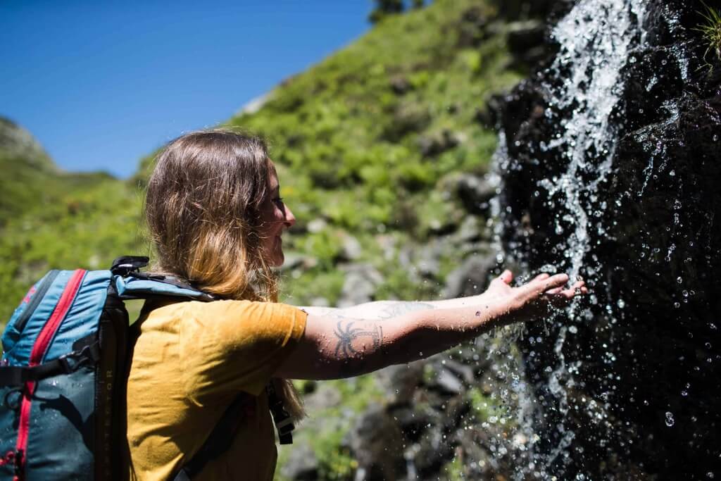 Wanderin in den Bergen, die Hand ausstreckend, um erfrischendes Wasser zu fangen.