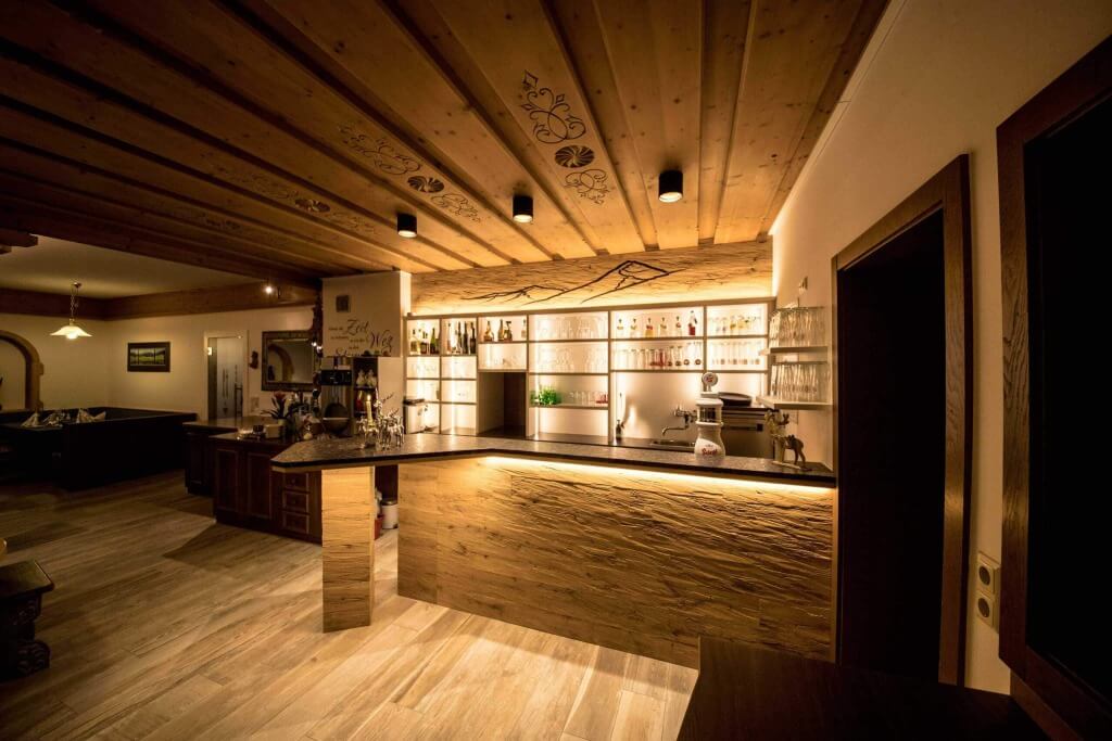 Gemütlicher Hotelbarbereich mit Holzregalen und beleuchtetem Tresen im Hotel Wolfgang.